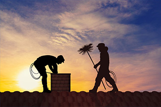 silhouetted image of workers on roof inspecting chimney and getting ready to sweep it